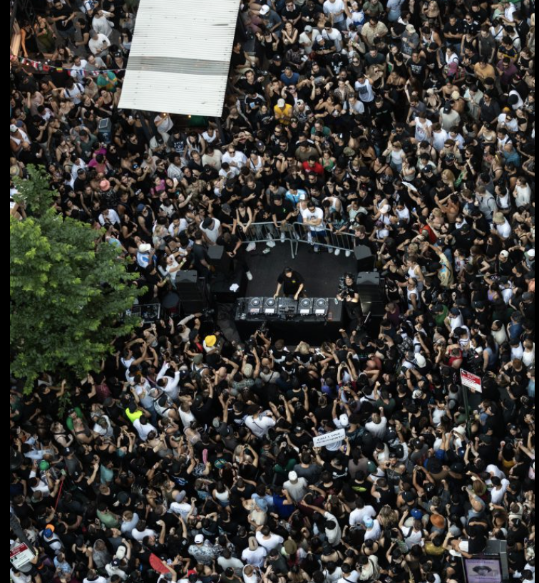Overhead aerial of NYC street pop-up rave, massive crowd around a DJ booth